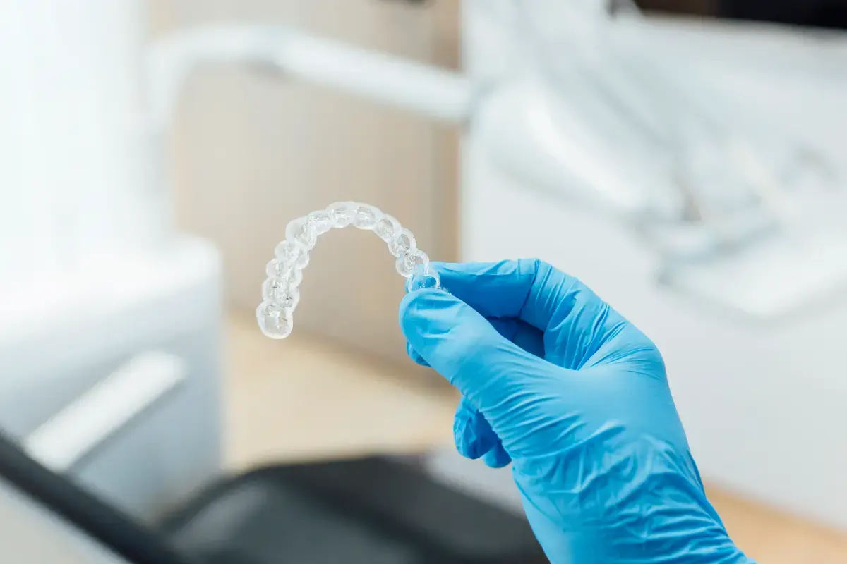 Gloved hand holding clear dental aligner in clinic.