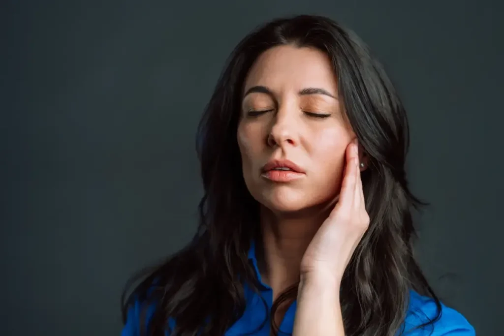 Woman in blue shirt with closed eyes, hand on cheek.